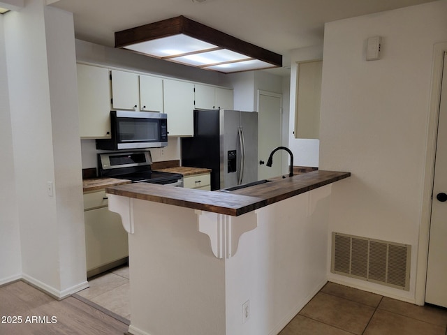 kitchen with butcher block counters, visible vents, appliances with stainless steel finishes, a sink, and a peninsula