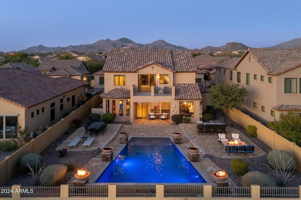 back house at dusk featuring a mountain view, a fenced in pool, pool water feature, a balcony, and a patio