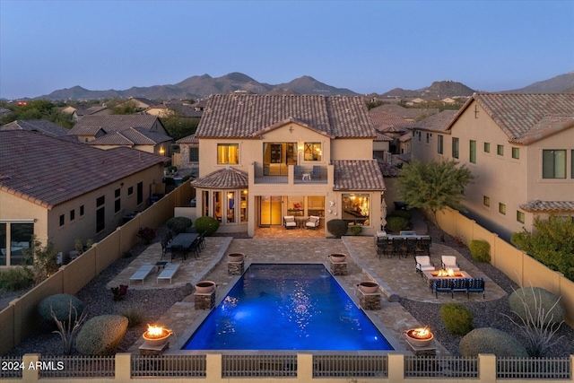 back house at dusk featuring a mountain view, a fenced in pool, pool water feature, a balcony, and a patio