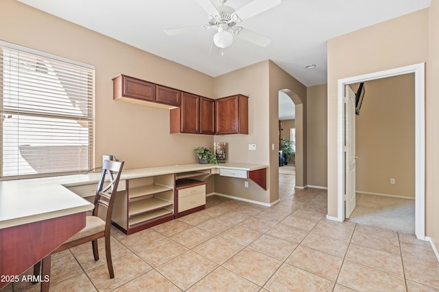 kitchen with light tile patterned floors, baseboards, arched walkways, a ceiling fan, and built in desk