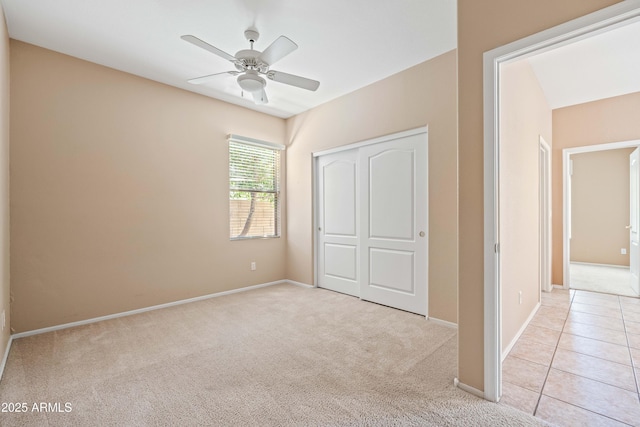 unfurnished bedroom featuring light carpet, light tile patterned floors, baseboards, a ceiling fan, and a closet