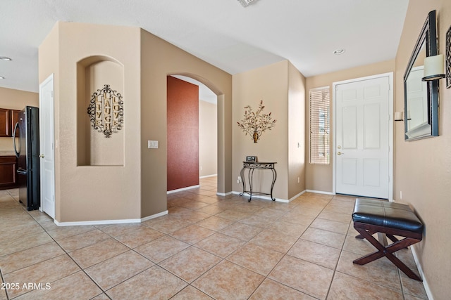 foyer with arched walkways, baseboards, and light tile patterned floors