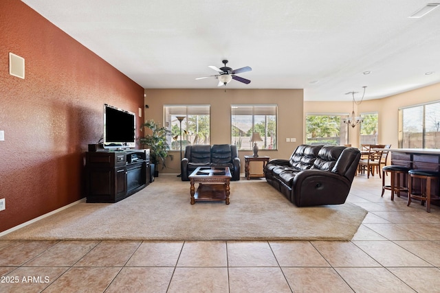 living area with light tile patterned floors, ceiling fan with notable chandelier, visible vents, and a textured wall