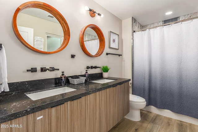 bathroom with double vanity, toilet, wood finished floors, a shower with curtain, and visible vents