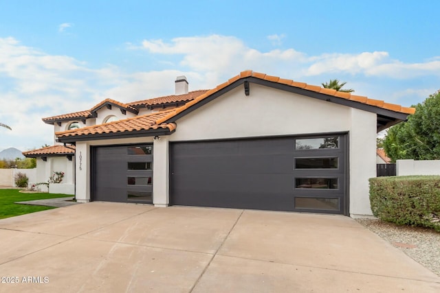 mediterranean / spanish-style home with fence, stucco siding, concrete driveway, an attached garage, and a tile roof