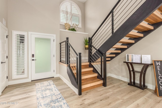 entryway featuring stairs, baseboards, wood finished floors, and a towering ceiling
