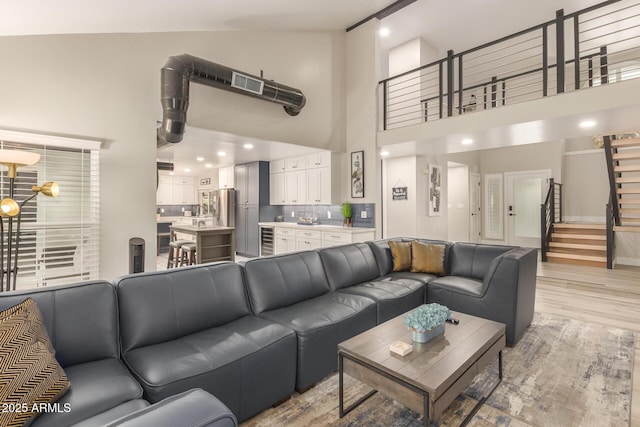 living area with light wood finished floors, beverage cooler, high vaulted ceiling, stairs, and visible vents