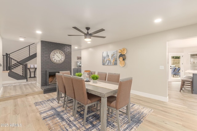 dining space with a fireplace, a ceiling fan, baseboards, light wood-type flooring, and stairway