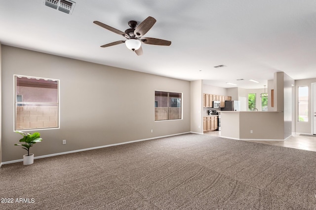 unfurnished living room with baseboards, visible vents, ceiling fan, and light colored carpet