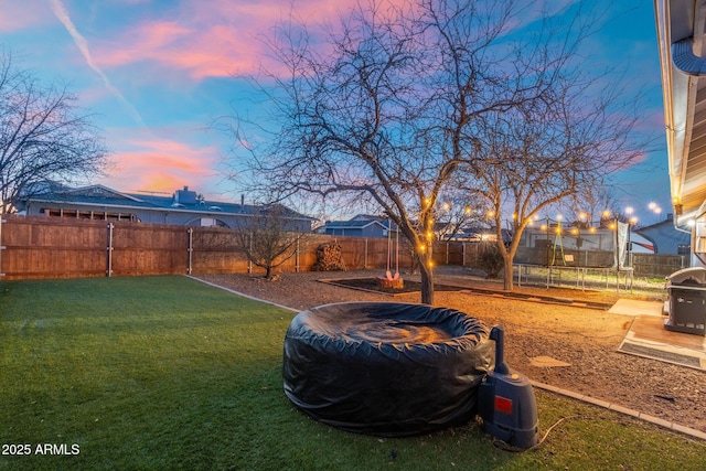 yard at dusk with a trampoline and a fenced backyard