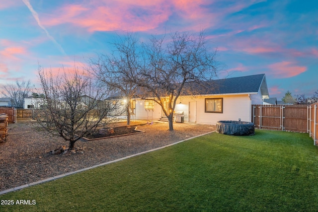 back of house at dusk featuring a fenced backyard and a yard