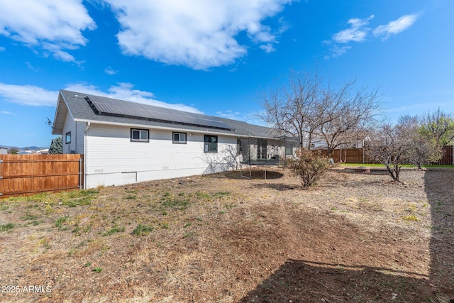 rear view of house featuring a trampoline, solar panels, and fence