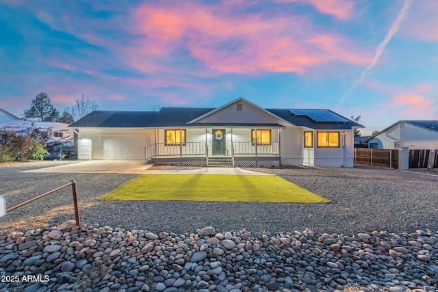 view of front facade featuring a front yard, covered porch, fence, solar panels, and a garage