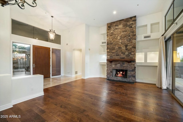 unfurnished living room featuring dark hardwood / wood-style flooring, a stone fireplace, an inviting chandelier, and a towering ceiling