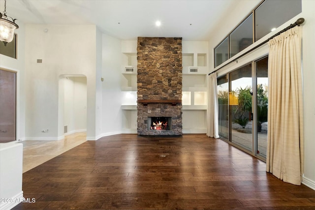 unfurnished living room featuring dark wood-type flooring, built in shelves, and a stone fireplace