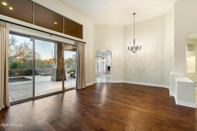 spare room featuring a towering ceiling, an inviting chandelier, and dark hardwood / wood-style floors