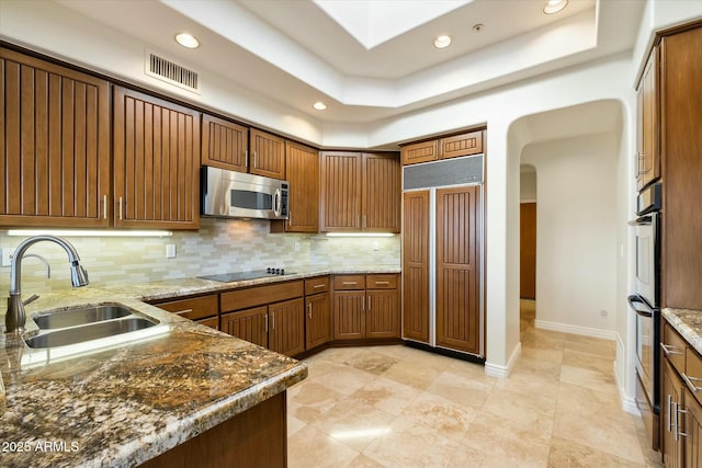 kitchen featuring light stone counters, tasteful backsplash, a tray ceiling, appliances with stainless steel finishes, and sink