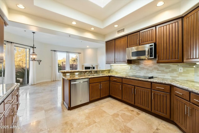 kitchen with appliances with stainless steel finishes, kitchen peninsula, pendant lighting, light stone counters, and decorative backsplash