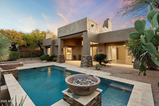 back house at dusk featuring a pool with hot tub, a patio, and a fire pit