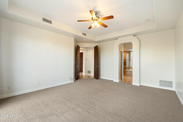 empty room featuring a raised ceiling, carpet floors, and ceiling fan