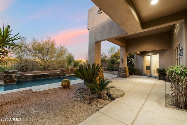 patio terrace at dusk featuring a fenced in pool