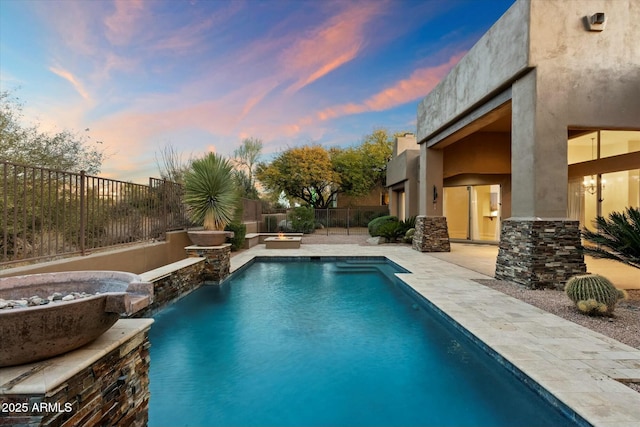 pool at dusk featuring a patio and pool water feature