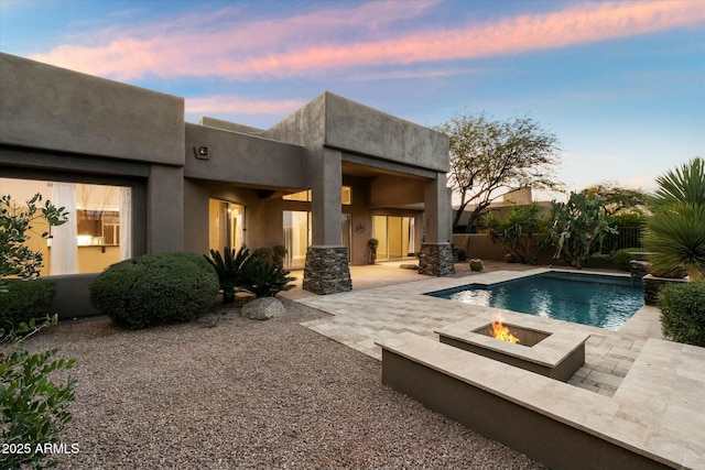 pool at dusk with an outdoor fire pit and a patio