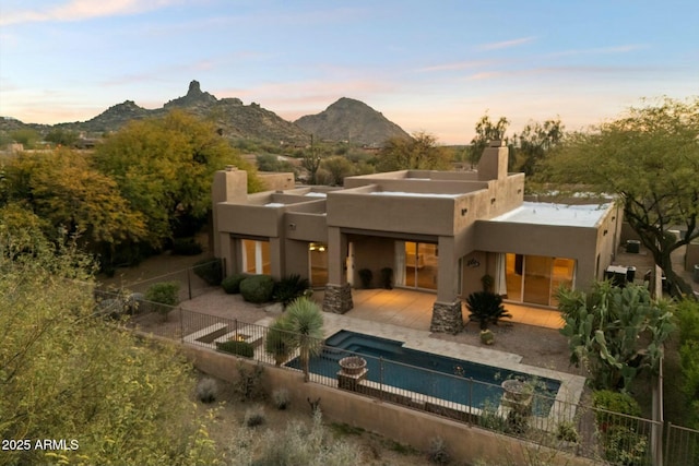 back house at dusk featuring a patio, a fenced in pool, and a mountain view