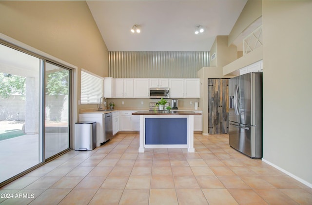 kitchen with a high ceiling, a kitchen island, a sink, white cabinetry, and appliances with stainless steel finishes