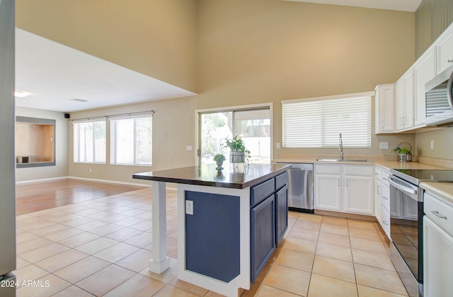 kitchen with appliances with stainless steel finishes, white cabinets, a sink, and light tile patterned flooring