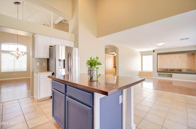 kitchen featuring light tile patterned flooring, stainless steel fridge, white cabinetry, and decorative light fixtures