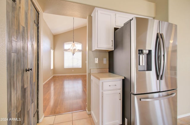 kitchen with stainless steel fridge, lofted ceiling, hanging light fixtures, light countertops, and white cabinetry