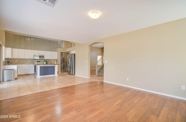 unfurnished living room with baseboards, visible vents, arched walkways, stairs, and light wood-style floors