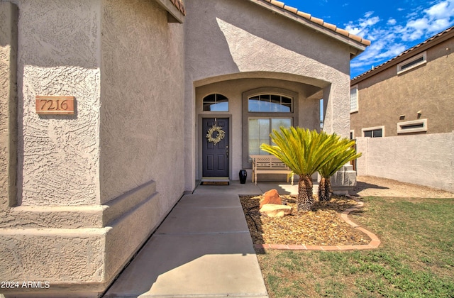 view of exterior entry with a tile roof, fence, and stucco siding