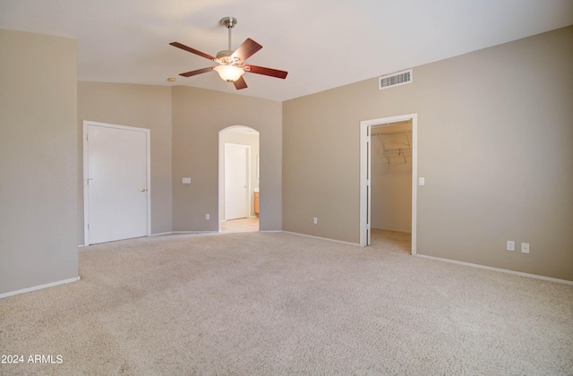 unfurnished bedroom with arched walkways, light colored carpet, visible vents, vaulted ceiling, and a spacious closet