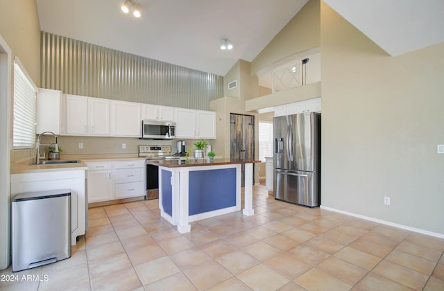 kitchen featuring white cabinets, appliances with stainless steel finishes, a center island, a sink, and light tile patterned flooring