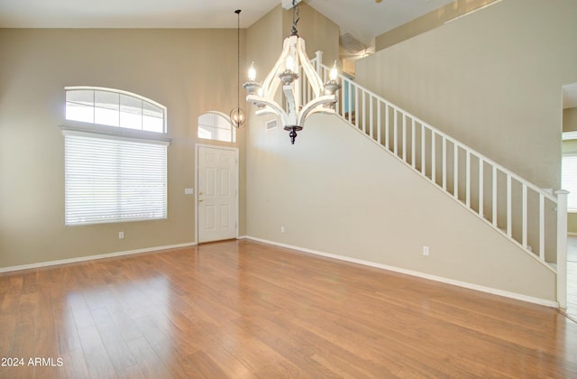 unfurnished room featuring stairway, a high ceiling, an inviting chandelier, wood finished floors, and baseboards