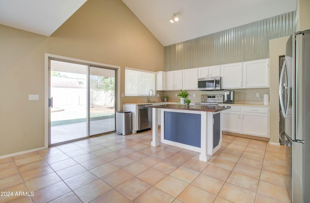 kitchen with light tile patterned floors, stainless steel appliances, white cabinetry, and a center island