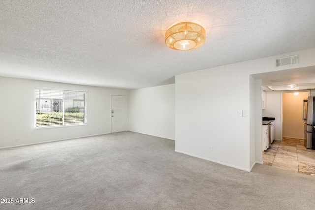 unfurnished room featuring light carpet, a textured ceiling, and baseboards