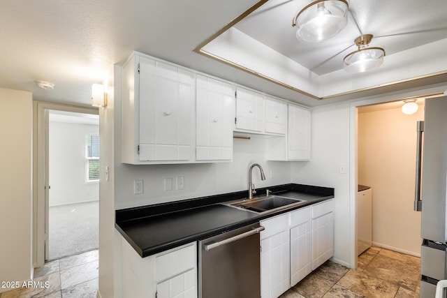 kitchen featuring appliances with stainless steel finishes, dark countertops, a sink, white cabinetry, and light stone finish flooring