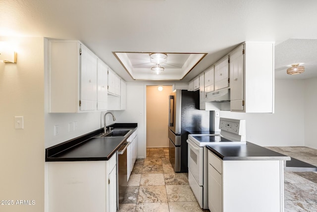 kitchen featuring white electric range oven, a sink, dark countertops, under cabinet range hood, and a tray ceiling
