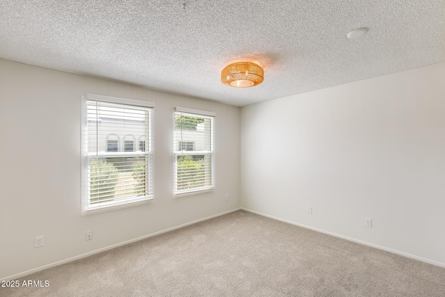 spare room featuring light carpet, baseboards, and a textured ceiling