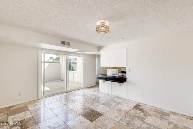 unfurnished room featuring a textured ceiling, baseboards, and stone tile flooring