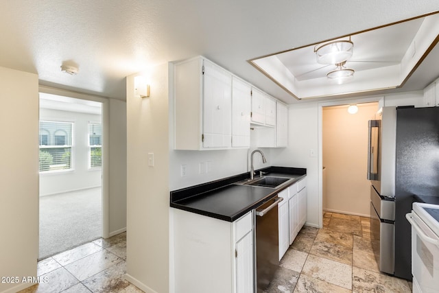 kitchen with stainless steel appliances, a sink, dark countertops, white cabinets, and a tray ceiling