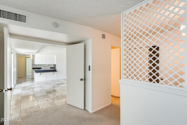 hallway featuring a textured ceiling, light colored carpet, and baseboards