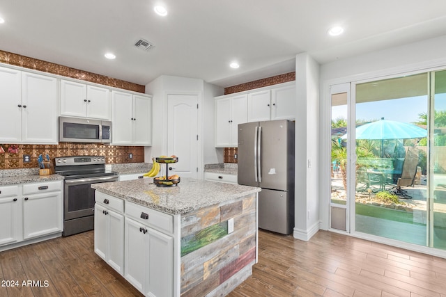 kitchen featuring hardwood / wood-style floors, light stone countertops, stainless steel appliances, and decorative backsplash