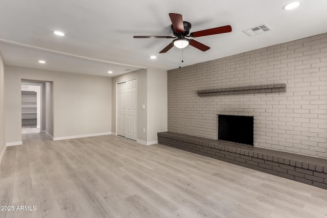 unfurnished living room featuring ceiling fan, a fireplace, brick wall, and light wood-type flooring