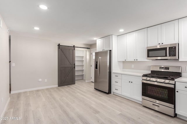 kitchen with white cabinetry, stainless steel appliances, a barn door, and light hardwood / wood-style floors