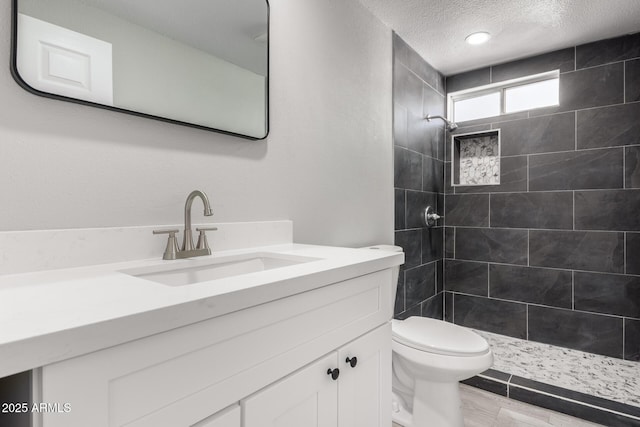 bathroom featuring vanity, toilet, a textured ceiling, and a tile shower