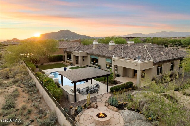 8599 E Sand Flower Dr, Scottsdale, AZ 85266 - back of property at dusk with a patio area, a chimney, a fire pit, a mountain view, and stucco siding